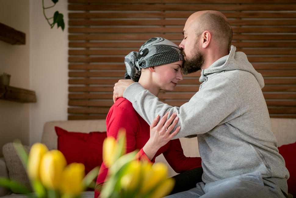 A young man kisses the forehead of a young woman in a head scarf.