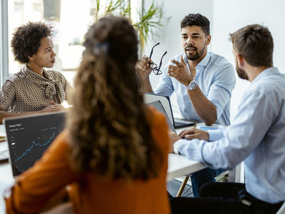 Team meeting with employees sitting at a table with their laptops open