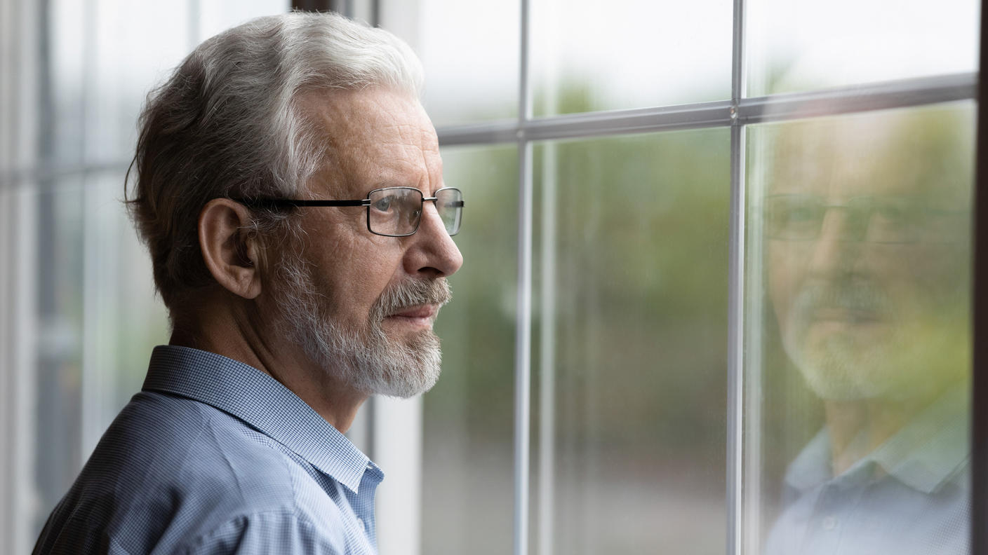 Senior man with glasses looking outside window.